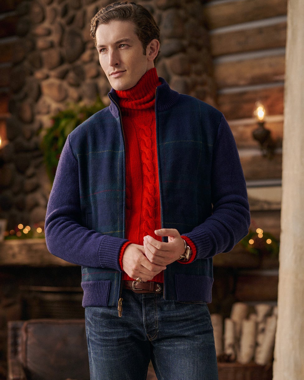 Homme portant un pull col roulé torsadé rouge, une veste marine et un jean.